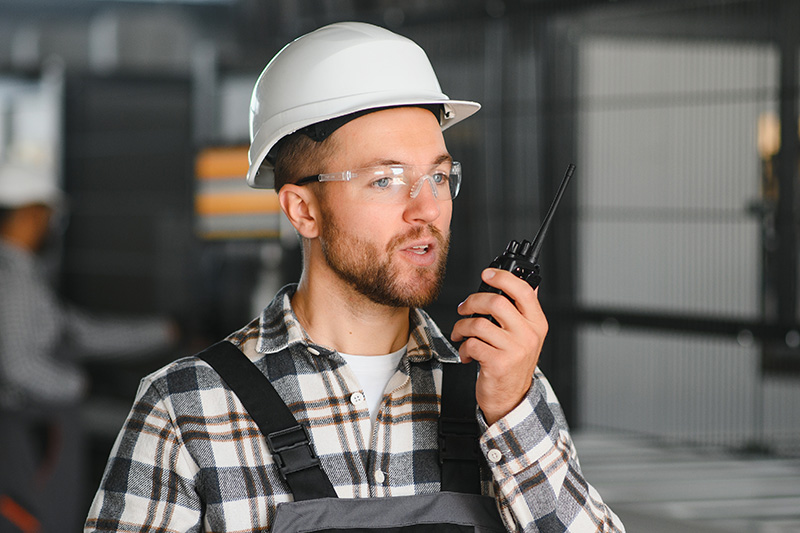 factory-worker-manufacturing-using-radio Factory worker utilizing a two-way radio to coordinate manufacturing operations.
