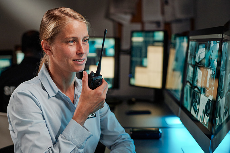 female-secutiry-officer-using-two-way-radio Female security officer using a two-way radio to coordinate safety measures in a commercial building.