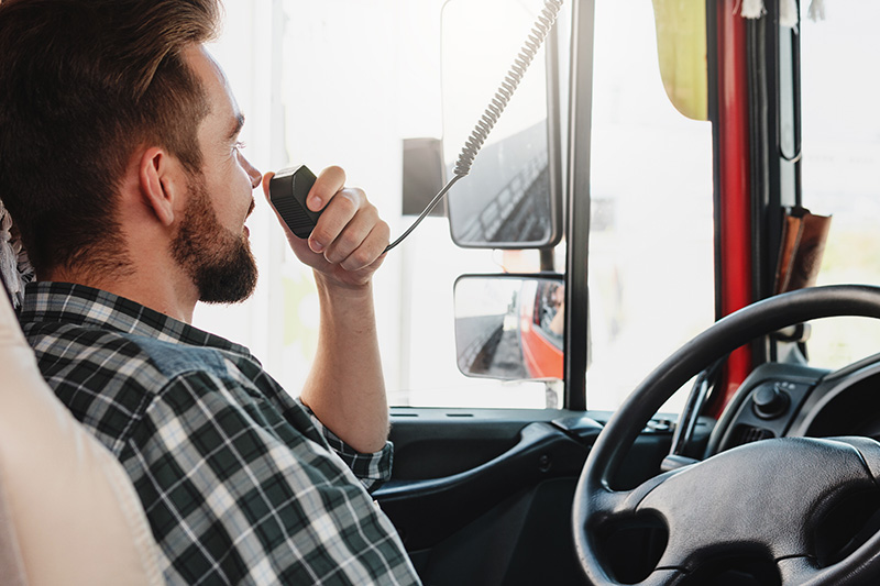 truck-driver-talking-by-radio Truck driver communicating via radio to ensure timely and coordinated deliveries.